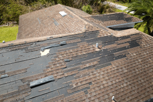 The image shows a roof with significant wind damage, featuring missing and displaced shingles. This highlights the need for professional wind damage restoration in Champaign, IL. The roof's condition underscores the importance of timely repairs to prevent further structural damage and ensure the safety of the property.