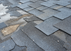 Close-up of damaged asphalt shingles on a roof showing signs of curling and water pooling, indicating potential leaks.