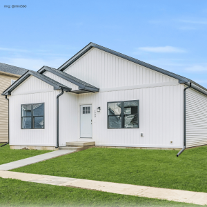 A modern single-family home featuring crisp white siding and contrasting black trim around windows and the roofline, set against a clear sky. The house has a minimalist design with a welcoming front door and a small front yard.